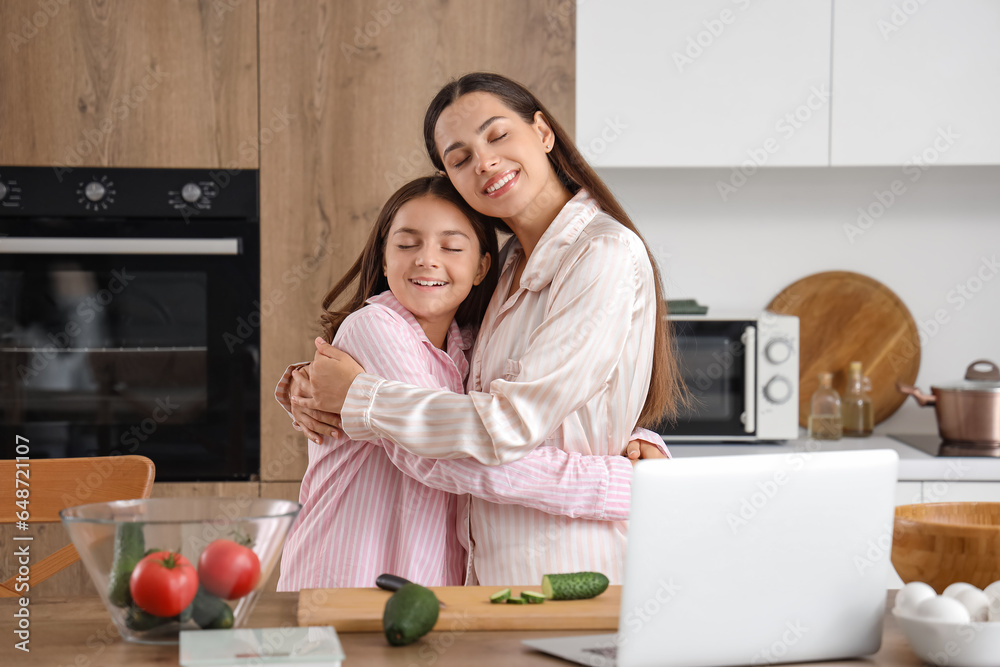 Happy mother with her little daughter hugging while cooking breakfast in kitchen