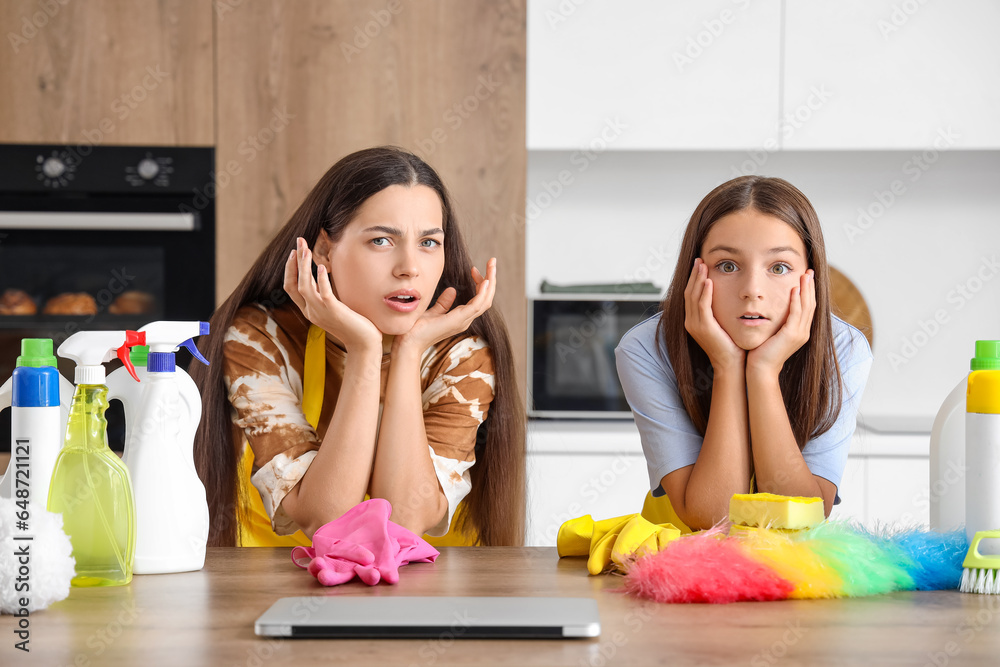 Shocked mother with her little daughter and cleaning supplies in kitchen