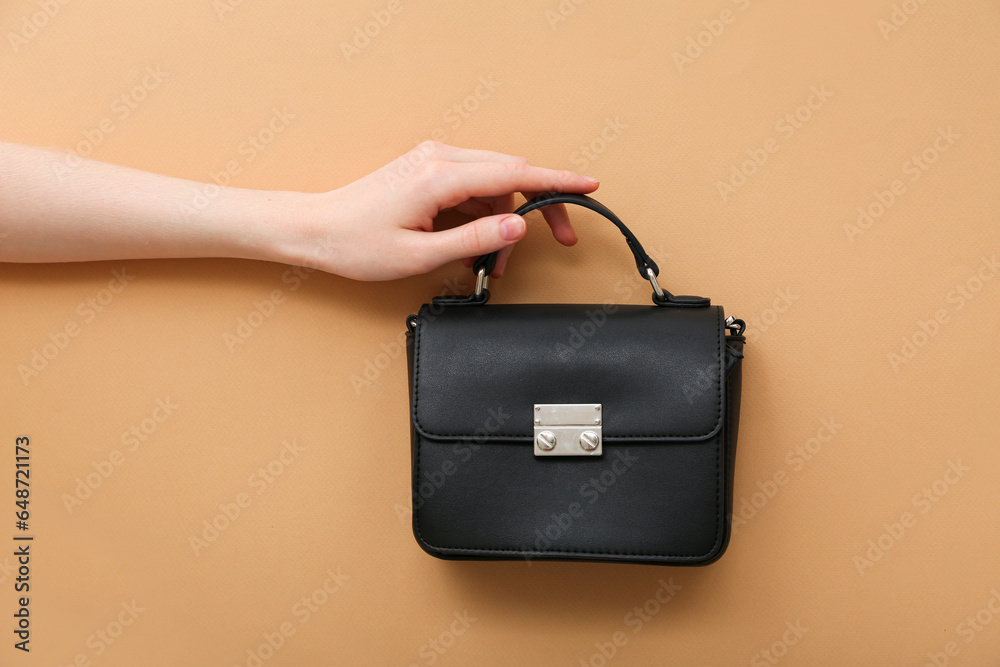 Female hand with stylish black handbag on brown background