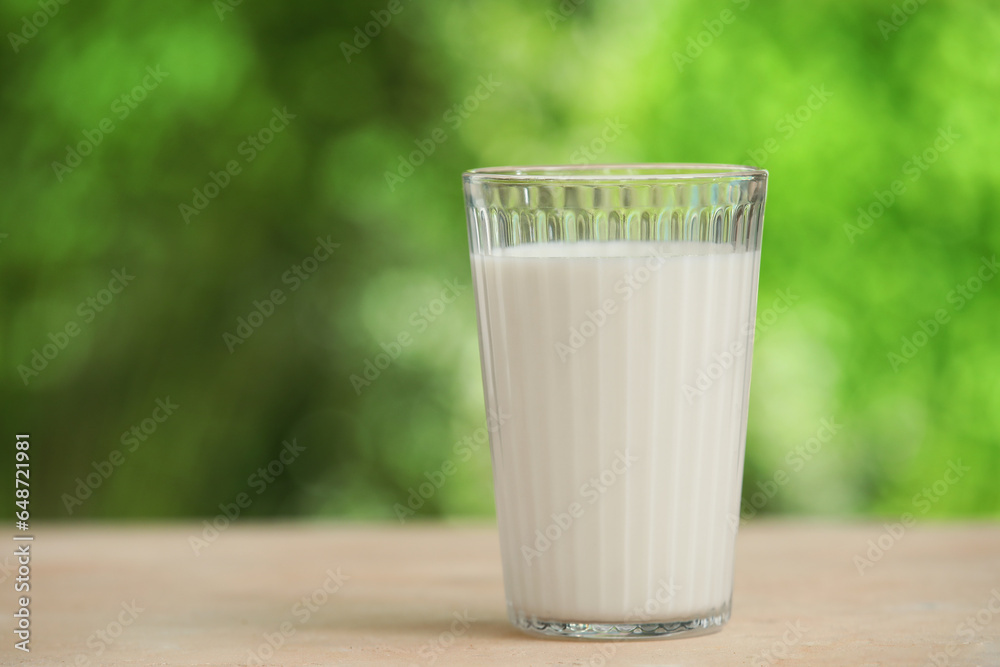 Glass of fresh milk on beige table outdoors