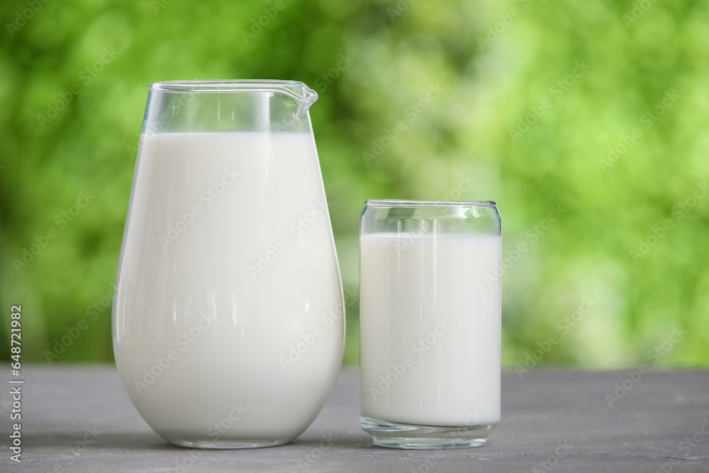 Glass and jug of fresh milk on grey table outdoors