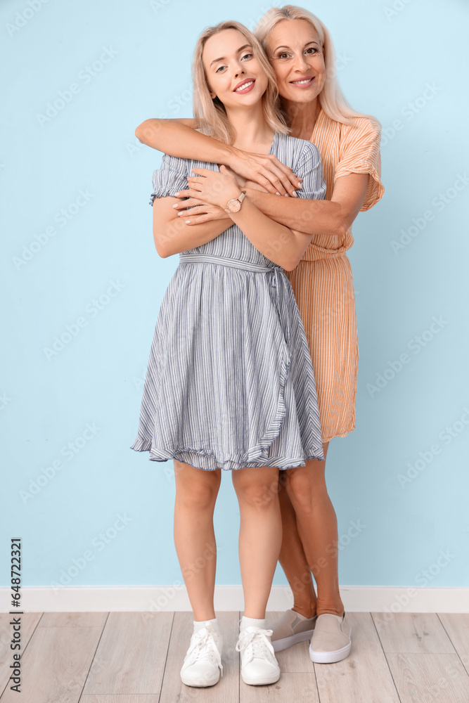 Happy young beautiful woman with her mother hugging near blue wall