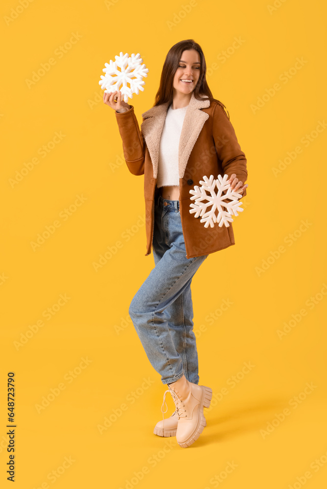 Young woman in winter clothes with snowflakes on yellow background