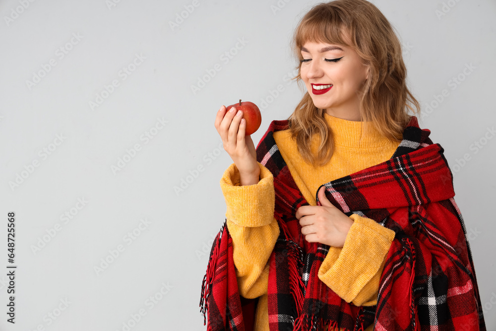 Young woman with plaid and apple on light background