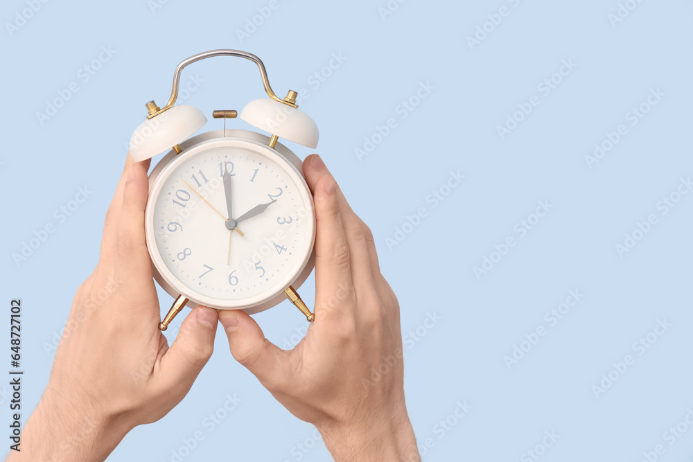 Male hands holding alarm clock on blue background