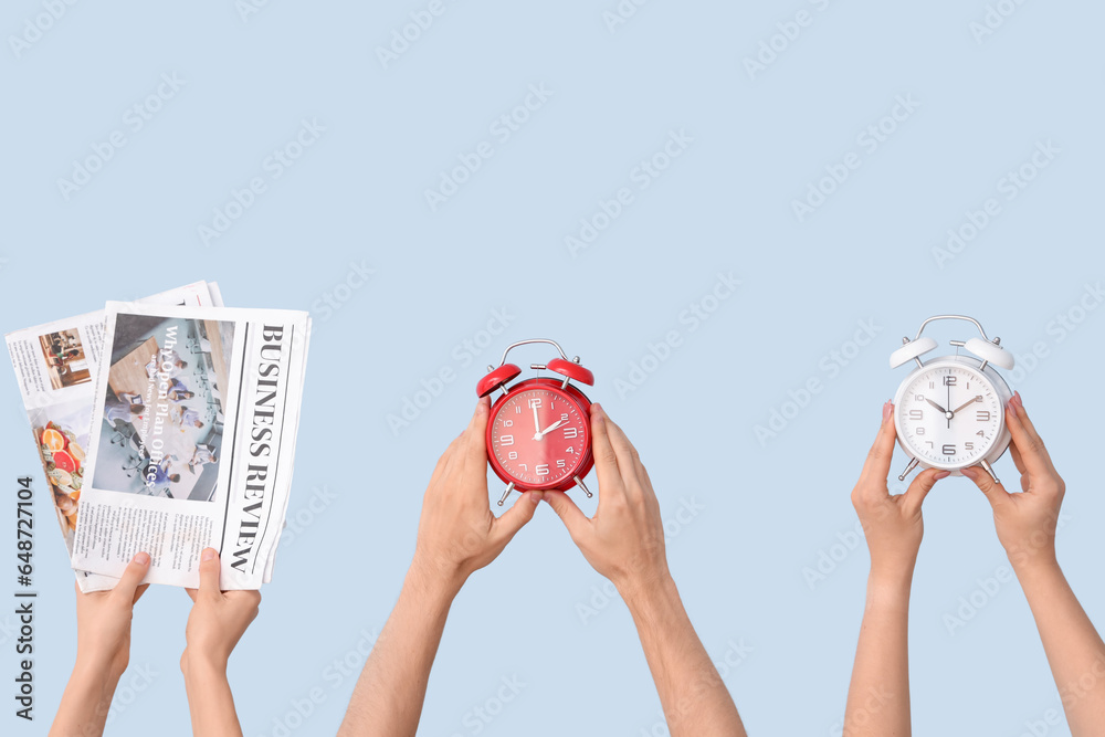 Hands holding different alarm clocks and newspapers on blue background