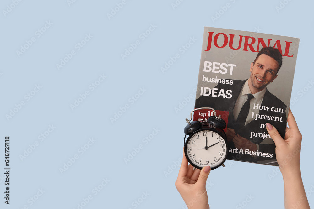 Female hands holding alarm clock and magazine on blue background