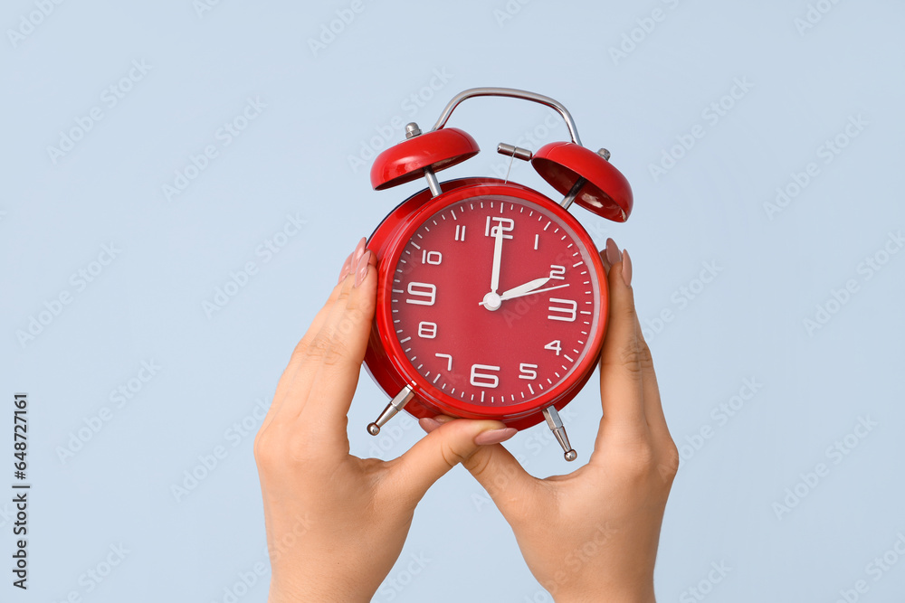 Female hands holding alarm clock on blue background