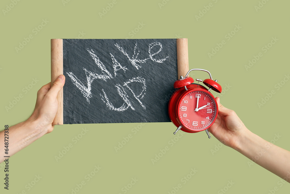 Hands holding alarm clock and board with text WAKE UP on green background