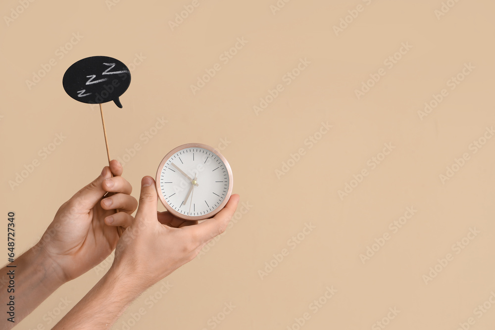 Male hands holding alarm clock and speech bubble on beige background