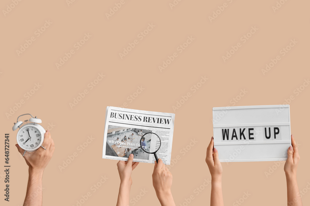 Hands holding alarm clock, newspaper, magnifier and board with text WAKE UP on beige background