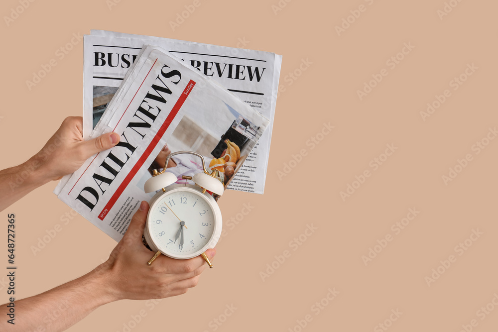 Male hands holding alarm clock and newspapers on beige background