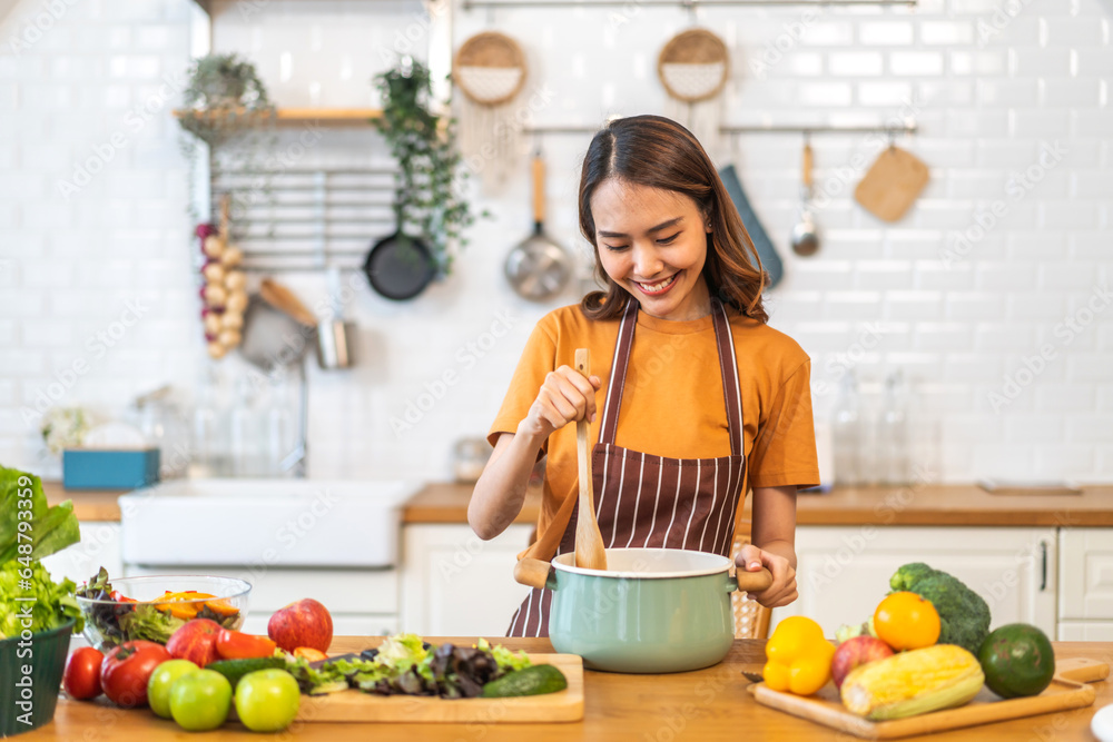 Young woman standing near stove and cooking, housewife, meal, chef, food.Happy woman looking and smelling tasting fresh delicious from soup in a pot with steam at white interior kitchen