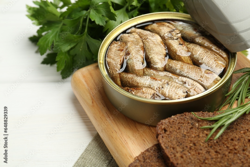 Canned sprats, herbs and bread on white wooden table, closeup. Space for text