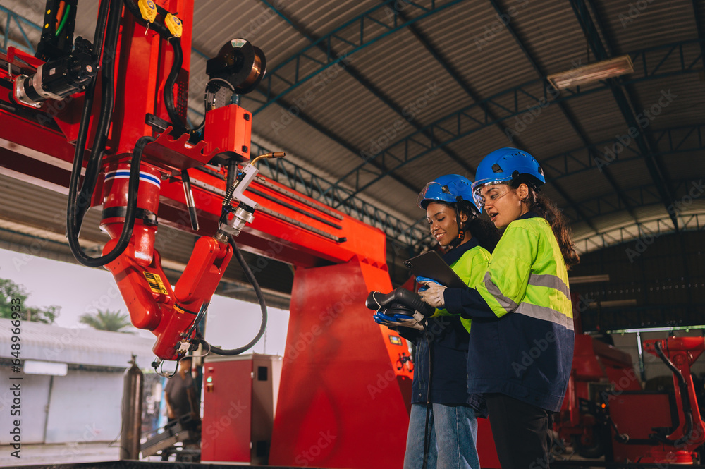 Female engineers work as a team training together in a modern technology world advanced robot welding machine factory.