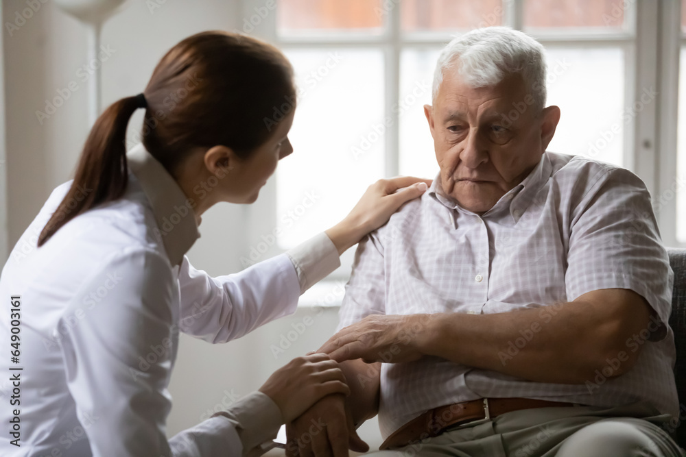 Caring female nurse or doctor talk support upset lonely mature 80s male patient in retirement house, supportive woman caregiver speak comfort unhappy sick old man, elderly healthcare concept