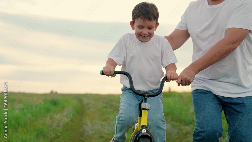 Childhood boy dream to ride bike. Dad teaches her little son to ride bicycle, sunset. Young father teaches child to keep balance while sitting on bicycle. Holiday family. Dad baby, Parental support