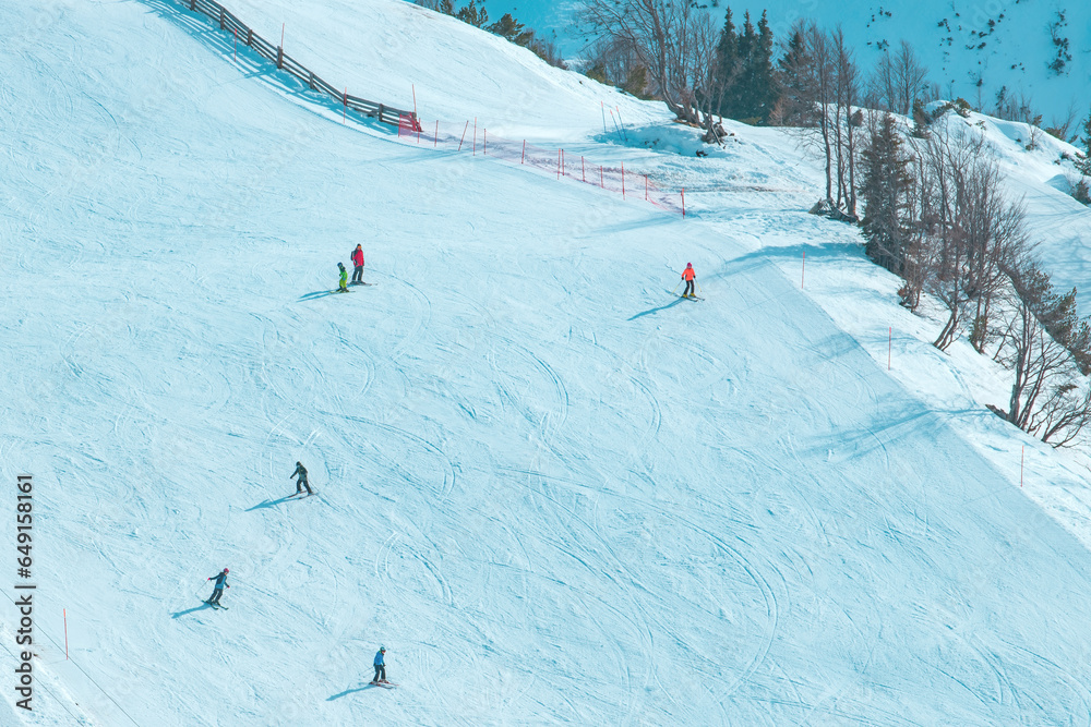 Large group of skiers enjoying sunny winter day on ski slope, unrecognizable people skiing