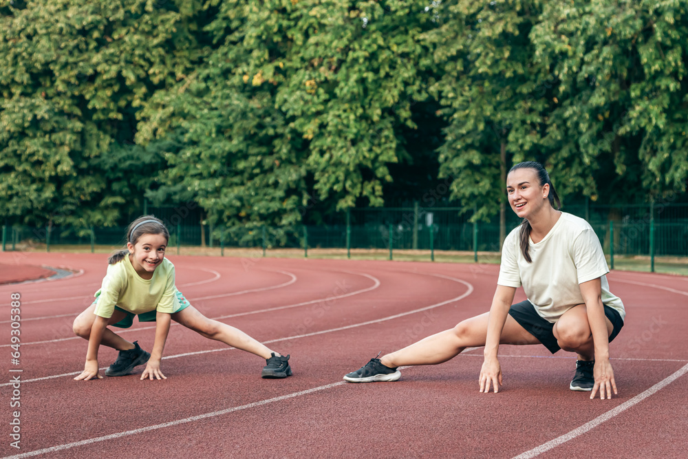 Mother and little daughter are doing exercise in the stadium.