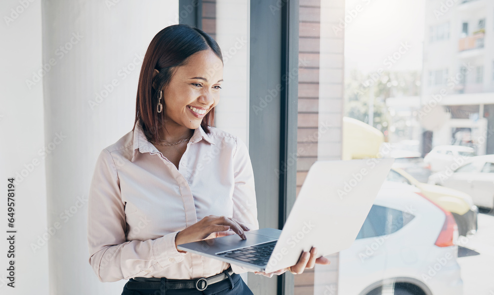 Woman in office with smile, holding laptop and reading email, HR schedule or online for feedback at window. Internet, networking and communication on website, happy person and human resources agency