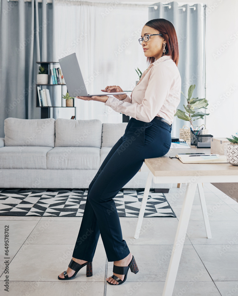 Laptop, typing and business woman at table in home living room on web research, networking and freelancer online. Serious designer on computer at desk, reading email and communication for remote work