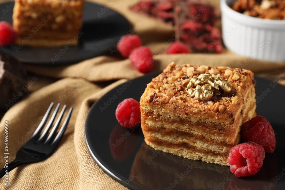 Pieces of delicious layered honey cake with nuts and raspberries served on table, closeup. Space for text