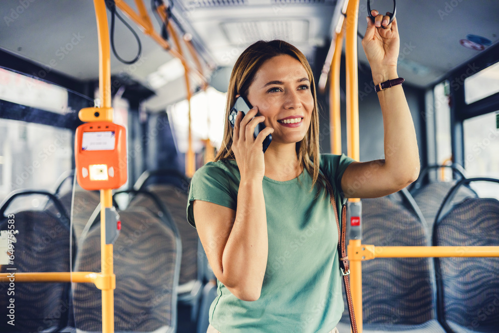 Beautiful young Caucasian woman who see a smart phone in city bus. Beautiful woman standing in city bus and using the phone. Businesswoman commuting to work by bus and working with a smartphone.