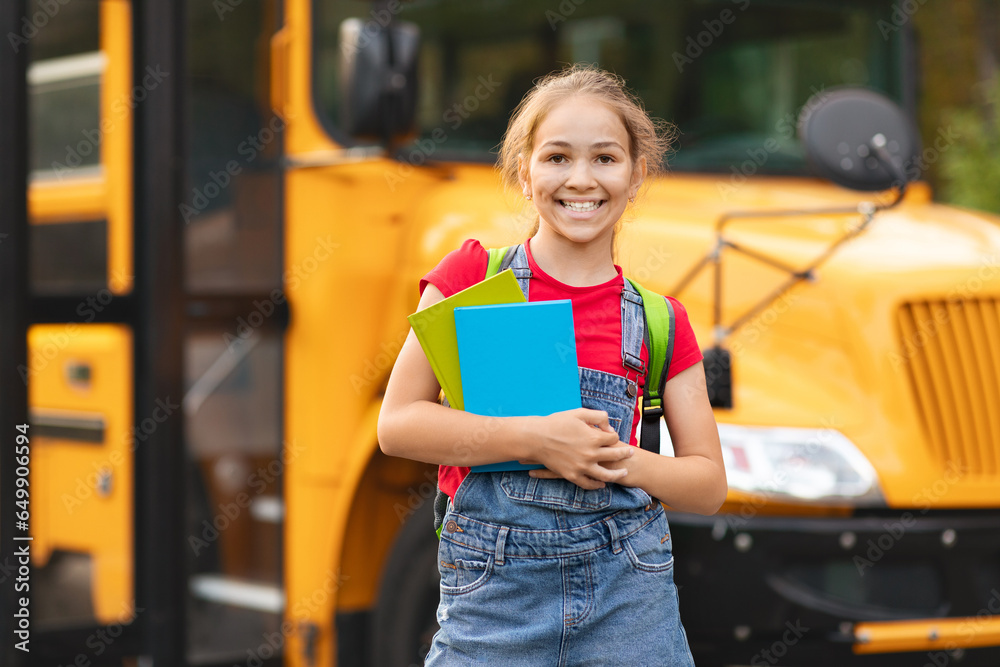 Back To School. Happy preteen girl with workbooks standing near school bus