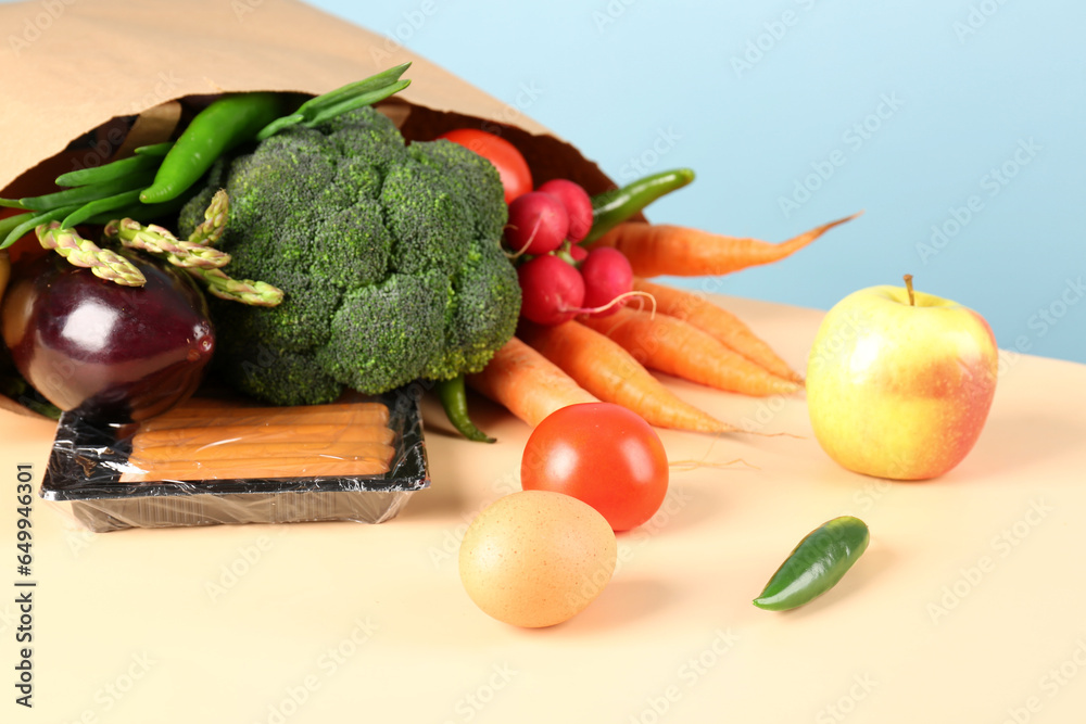 Paper bag with vegetables, fruits and sausages on table