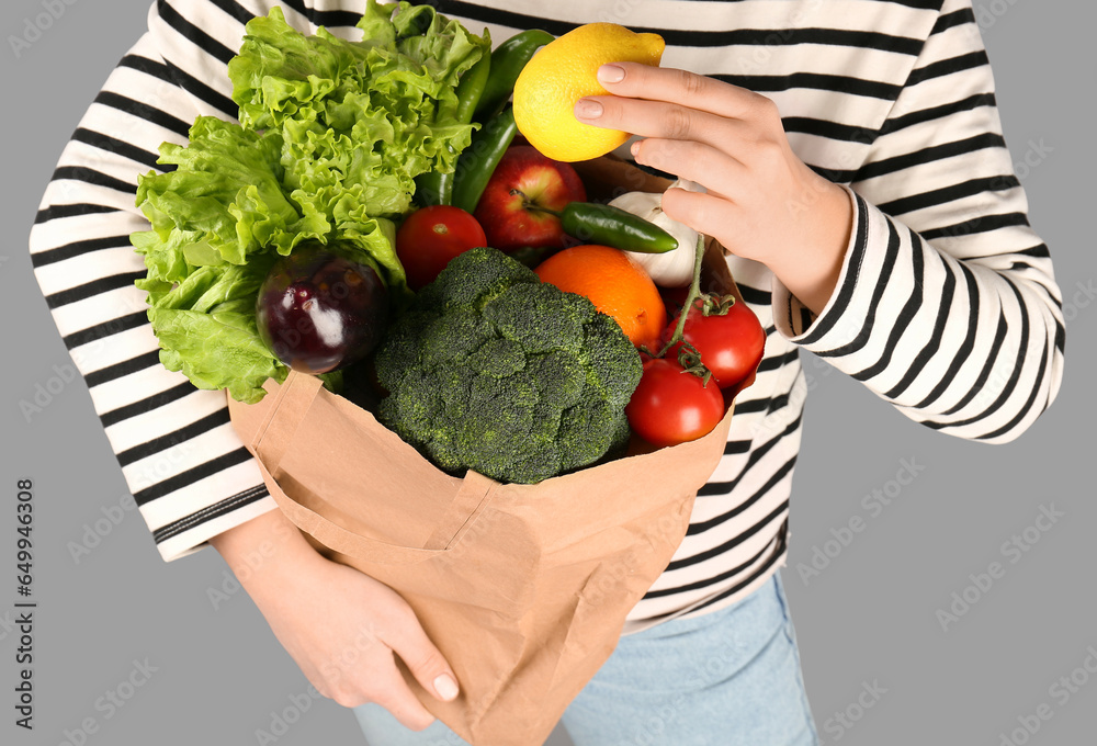 Woman holding paper bag with vegetables and fruits on grey background