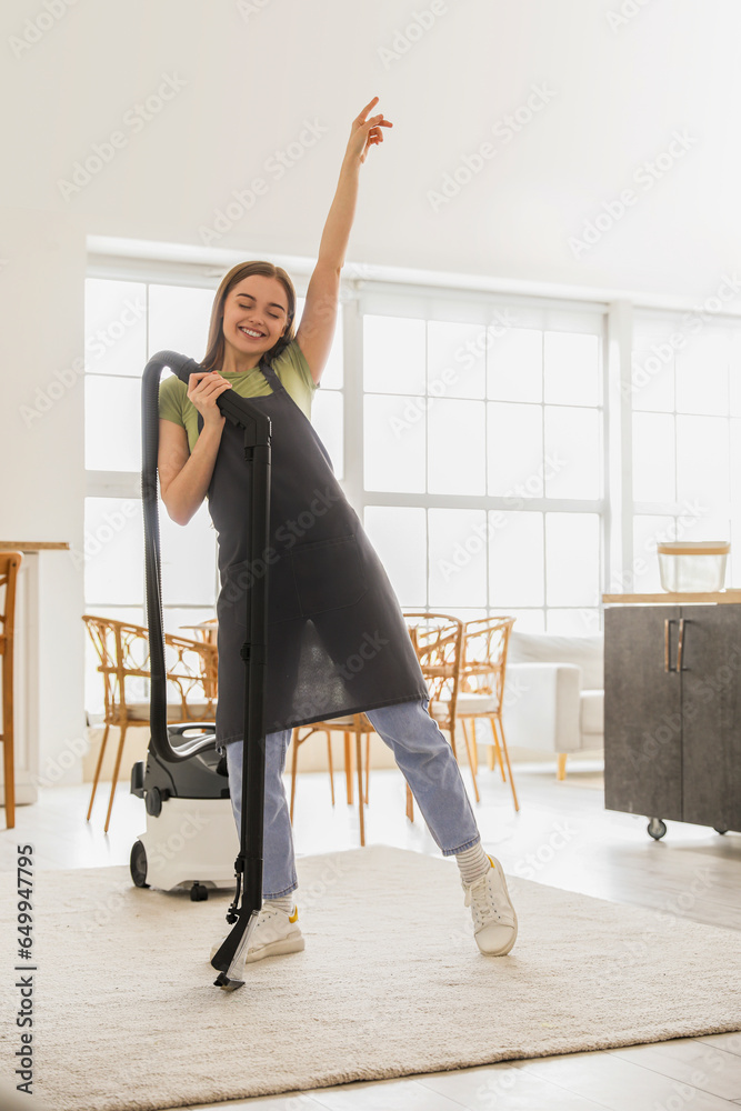 Young woman with vacuum cleaner dancing in kitchen