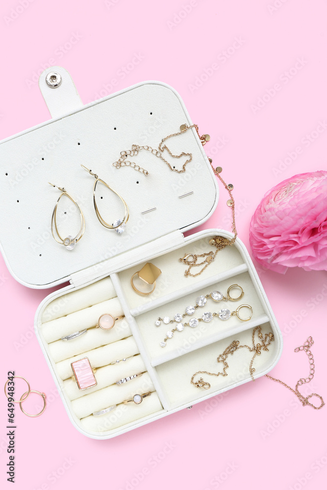 Opened organizer with stylish jewelry and flower on pink background