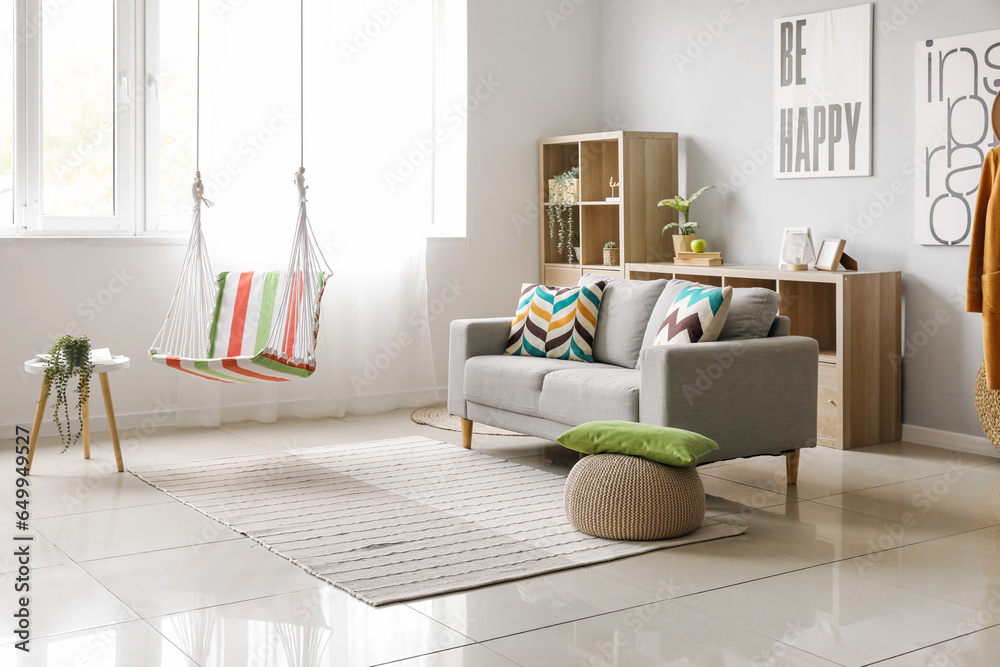 Interior of stylish living room with striped hammock and grey sofa