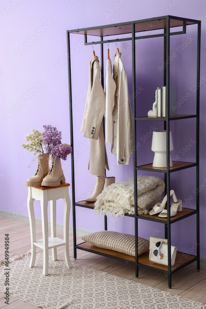 Interior of stylish room with shelving unit, clothes and stool