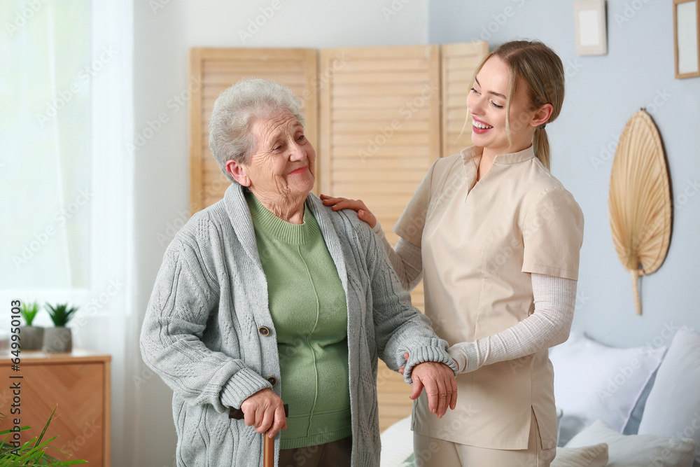 Young caregiver helping senior woman in bedroom