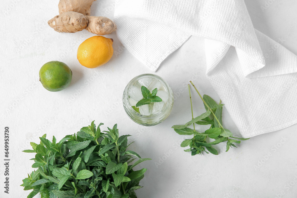 Glass of fresh icy mint tea with ginger root and citruses on white background