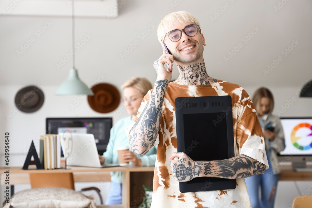 Male graphic designer with tablet talking by mobile phone in office