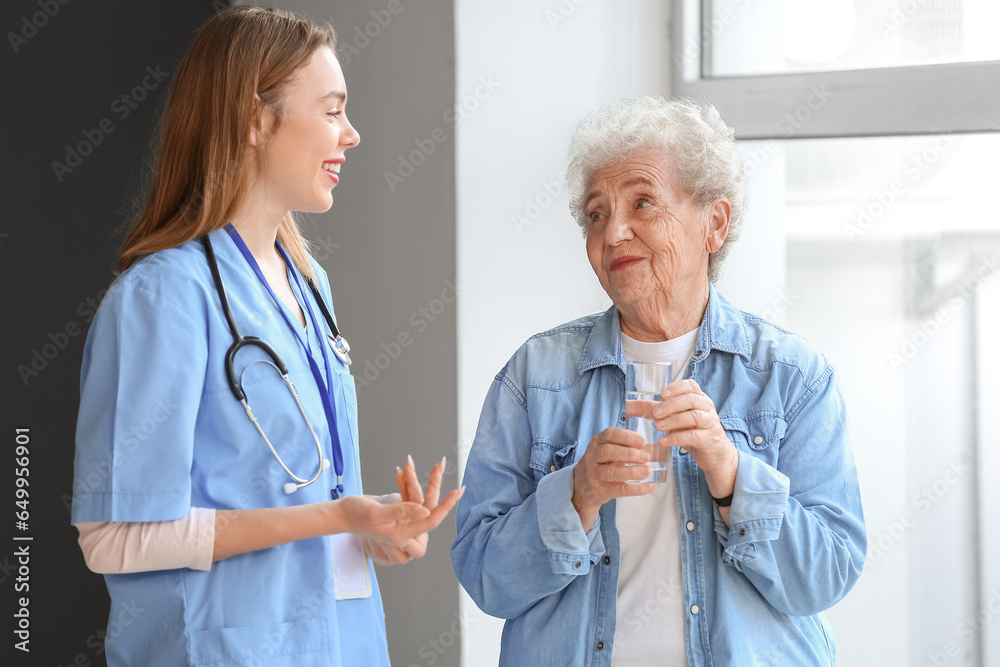 Senior woman with glass of water and female caregiver in room