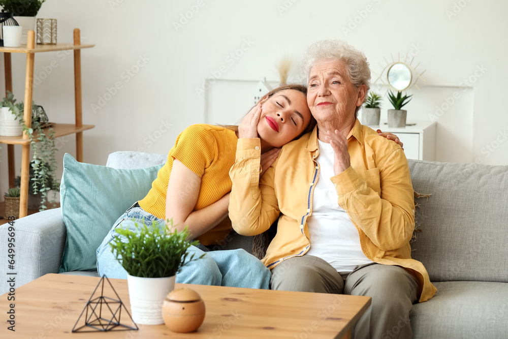 Young woman with her grandmother hugging on sofa at home