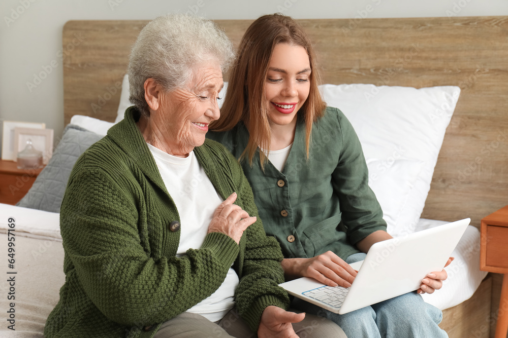 Young woman with her grandmother using laptop in bedroom