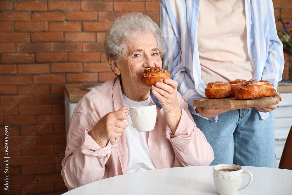 Young woman with her grandmother eating buns in kitchen