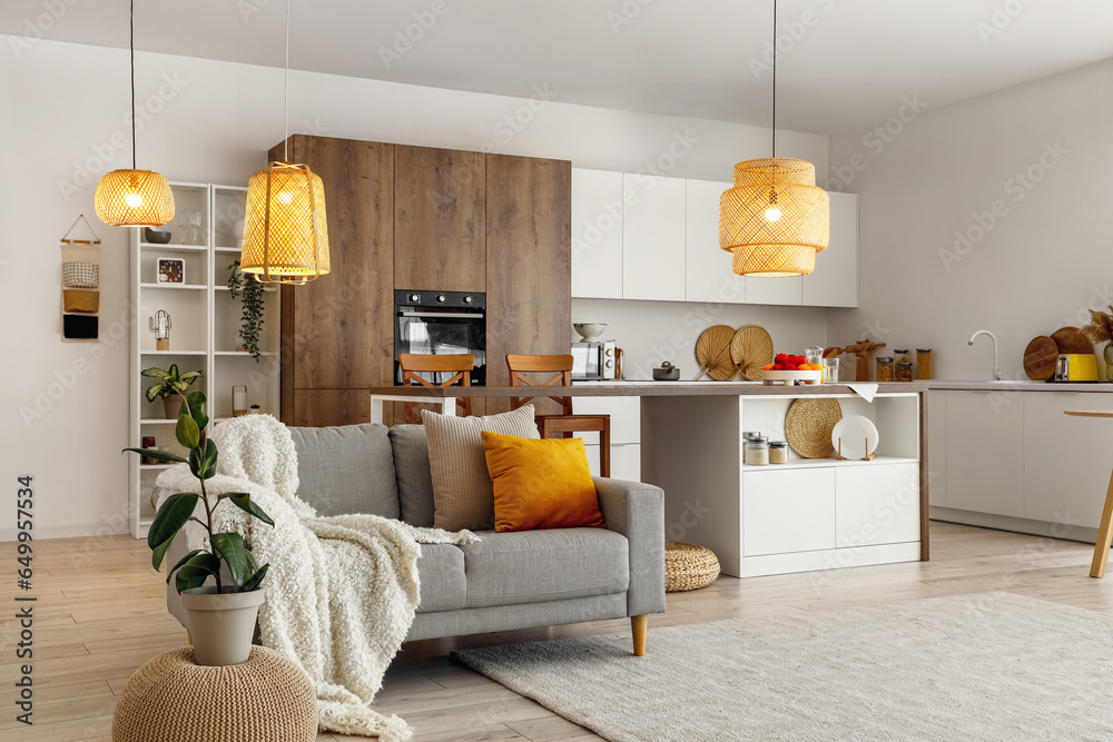 Interior of modern open plan kitchen with island table, grey sofa and glowing lamps