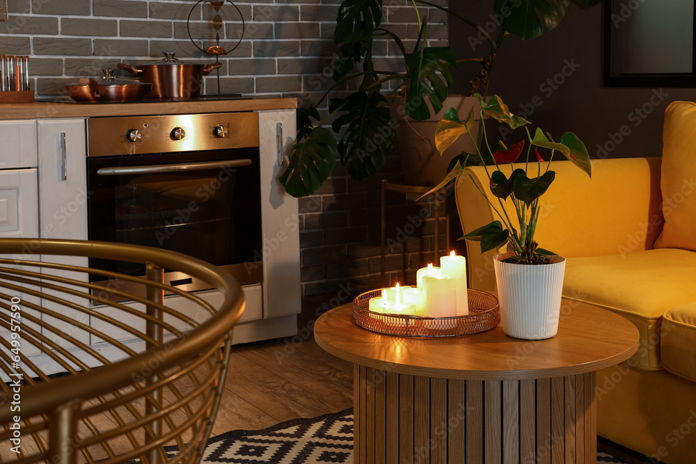 Interior of modern kitchen with yellow sofa and burning candles on wooden coffee table at evening