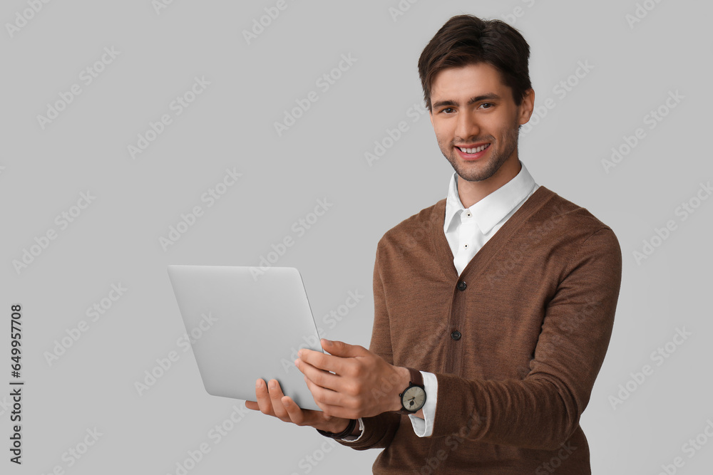 Handsome stylish young man with wristwatch and laptop on grey background