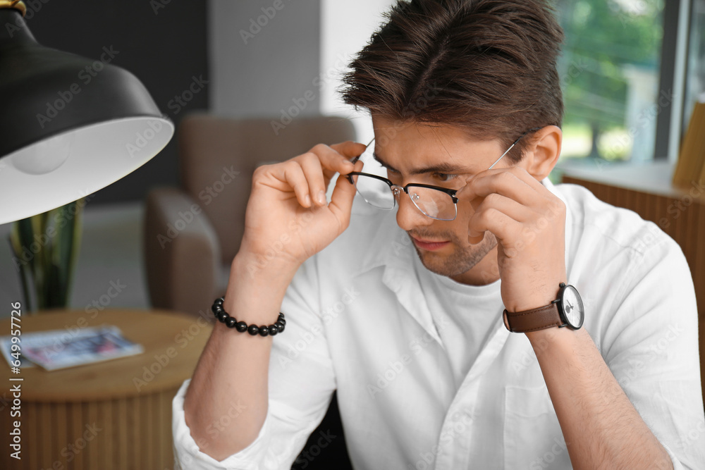 Stylish young man with wristwatch and eyeglasses sitting in office