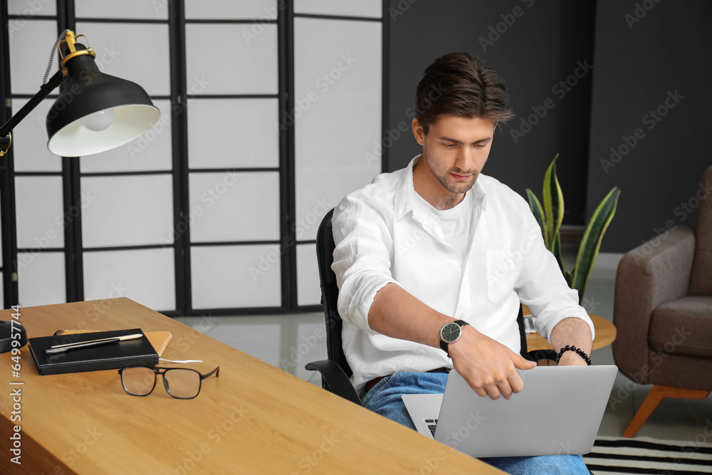 Handsome young man with wristwatch working on laptop in office