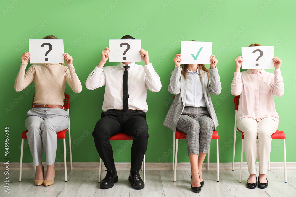 Young applicants holding paper sheets with check and question marks in room