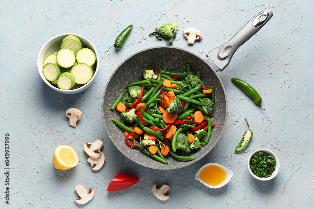 Frying pan with fresh vegetables on grey background