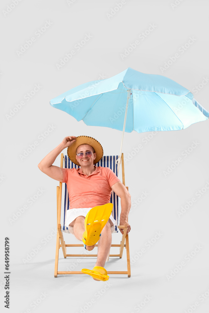 Mature man relaxing in deck chair on light background