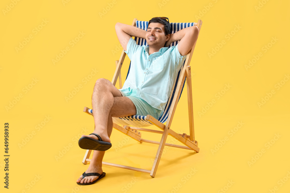 Young man relaxing in deck chair on yellow background